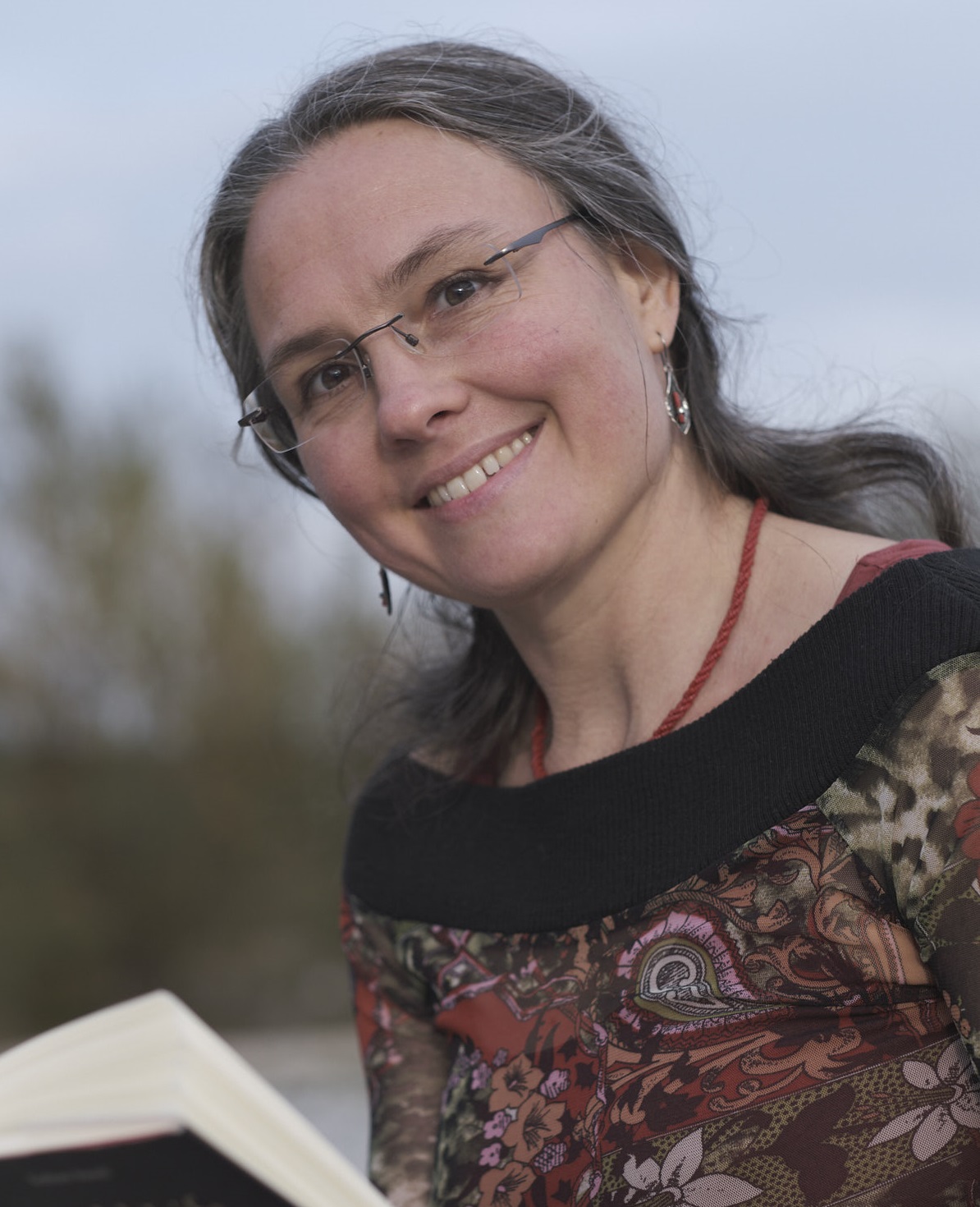 Dr. Friederike Kleinknecht, Paar- und Sexualberaterin aus Innsbruck, lächelt beim Lesen eines Buches im Freien - offen, herzlich und nahbar.